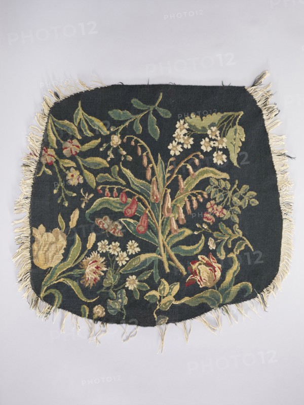 Tapestry covering, Leaves and floral ornaments; decorative fabric for interior furnishings. Design: a Seat — bouquet of lily of the valley in the center with sprigs of other flowers including tulips; b Backrest — lily flowers in the center with sprigs of other flowers including irises. Colors: dark green. Materials: fabrics. Date: 1st half of the 20th century. Place of origin: Vienna. Dimensions: height 68 cm, width 72 cm., A rectangular textile with rounded corners and fringe along the edges lies flat against a pale background; the textile has a dark background with a floral tapestry design featuring a variety of stylized flowers and leaves in colors including green, yellow, cream, red, and brown, with cream-colored fringe around the perimeter.