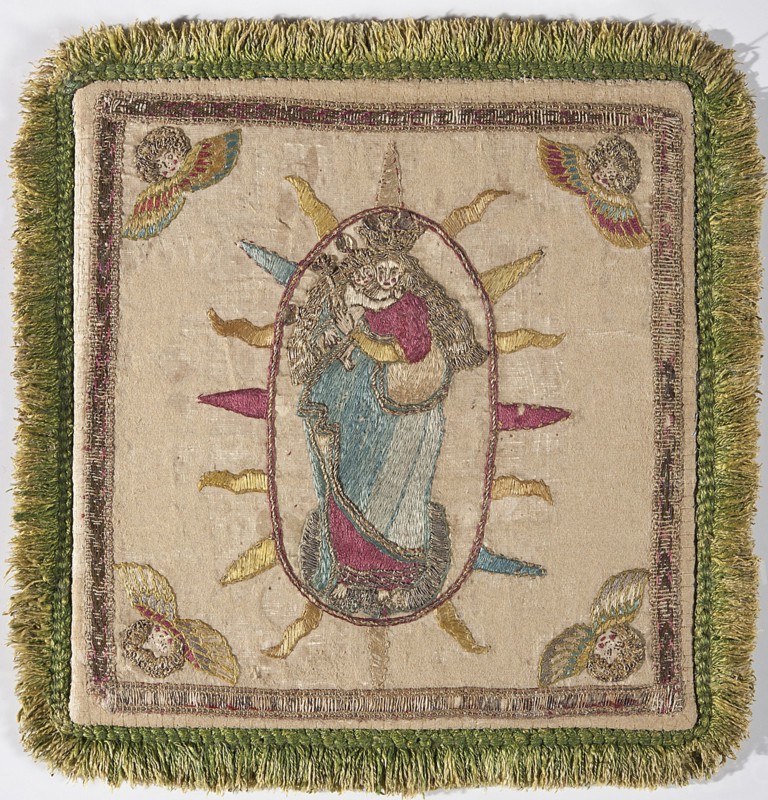 Pall, Madonna and Child iconography. Embroidery; church paraments; palls; angel heads ornament. Poland. Chalice cover made of cream satin, embroidered with colorful silk yarn, gold and silver metal thread, and sequins. In the center, in a radiant oval, Mary wearing a crown, holding the Child and a scepter, standing on a globe. In the corners are winged angel heads. Pall trimmed with narrow braid and green shreds. Flat embroidery on small thread underlays, executed with silk yarn and metal-braided threads on a silk base, decorated with silver-gold paillettes. Colorful embroidery using split and satin stitches, and gold embroidery using a laid stitch. Angels' hair is made of metal threads arranged in loops and held together with silk yarn. 18th century, Poland. Liturgical vestment, fabrics. Height 20 cm, width 19.5 cm., A square textile panel with a fringed border in shades of green surrounding an inner embroidered border in gold and muted pink, the central field in a beige or cream fabr...