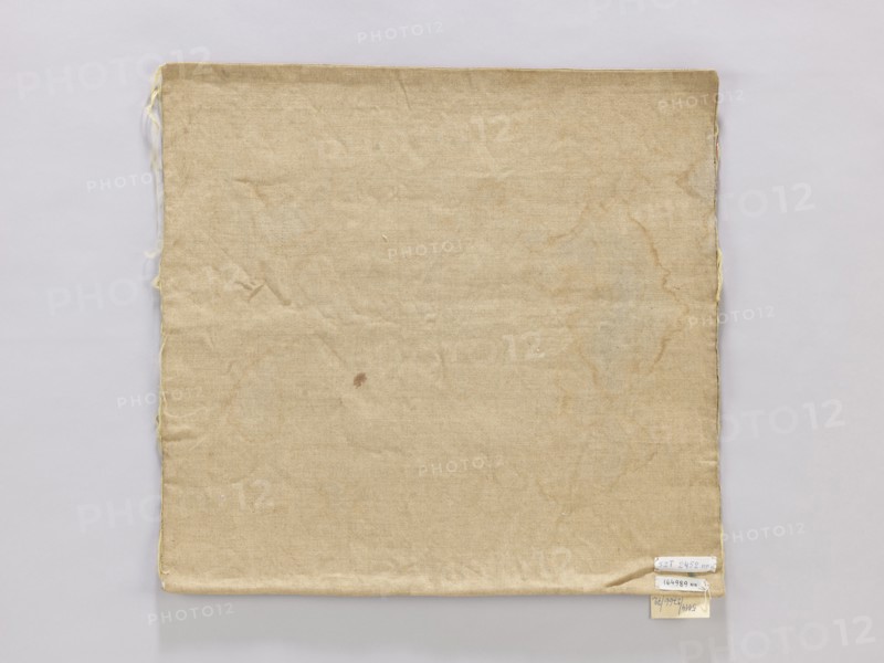 Vellum, church paraments, vellum, plant ornaments, unknown origin, 19th century, Poland, liturgical parament, height 44 cm, width 42 cm, A square piece of fabric with a worn, creased surface occupies most of the image, showing a beige to tan color with slightly darker brownish stains and discoloration in irregular patterns; the fabric has frayed edges along the left and right sides with a few loose threads visible, and the bottom right corner is slightly folded and layered over a pale background that is light gray to off-white.