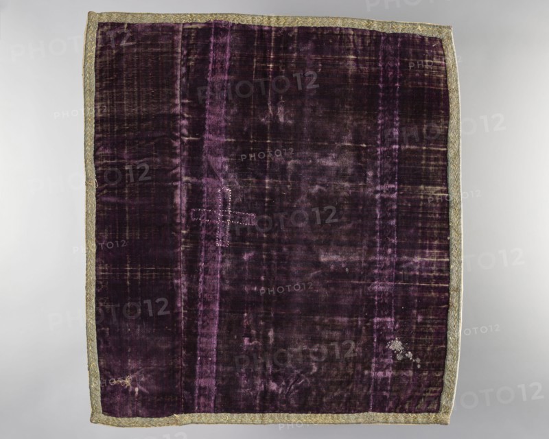 Velum;, church paraments; revindication provenance; flowers; plant ornaments; sacred art; churches and chapels furnishings; 18th century, Italy; liturgical parament; height 46 cm; width 51 cm, A rectangular textile laid flat with a deep purple velvet field showing areas of lighter purple sheen and worn darker patches, bordered all around by a narrow metallic trim in a muted gold-green tone; the velvet surface has visible vertical banding and a few irregular worn spots, including one area with a pale cluster of abrasion and another small rubbed area, and there is a stitched cross-shaped repair in a slightly lighter purple thread near the upper left quadrant.