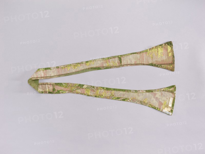 Stole made of Lyon material, early 18th century, Lyon, France; liturgical vestment with plant ornamentation—flowers and leaves; used as church parament; length 158 cm, width 16 7 cm., A long, narrow fabric strip with wider triangular ends laid flat on a pale background, showing a patterned woven surface with visible texture and frayed edges; the fabric displays shades of green and pink with accents of yellow and hints of beige and metallic sheen.