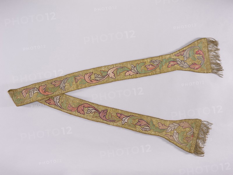 Stole, church paraments; flowers; liturgical vestments; plant ornaments; sacred art; churches and chapels furnishings. Stole embroidered with a leafy twig motif in silver, green, and two shades of pink. Gold fringe sewn to the ends of the paddles. See manipular inventory number SZT 2449. 17th/18th century, Poland. Liturgical vestment. Length 212 cm, width 19 cm., A long decorative textile laid flat in a diagonal arrangement with a few fringed ends, showing an embroidered scrolling leaf-and-flower pattern; the textile has a dominant gold background with visible areas of pink, green, pale blue, and muted purple in the ornamental motifs, and the fringes appear goldish-beige.