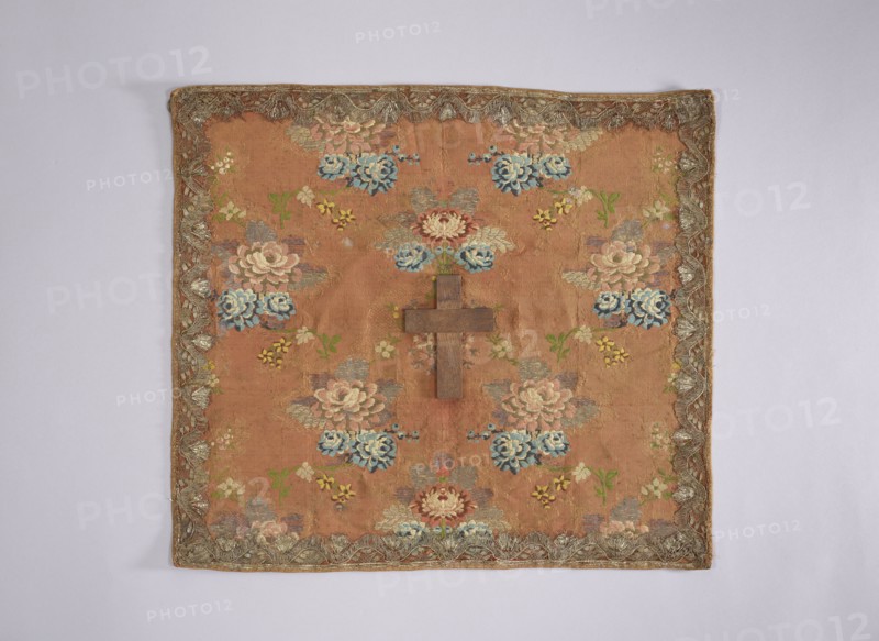 Velum; creator, Rómmel Jadwiga gift, provenance; church paraments; flowers, leaves, plant ornaments; sacred art; churches and chapels furnishings; 2nd half of the 18th century; France; liturgical parament; height 47 cm, width 53 cm, A square textile with a warm brown background decorated with a repeating floral pattern in shades of blue, pink, cream, green, and yellow, featuring several stylized blossoms and leafy sprigs; a wooden cross in a darker brown is placed near the center; the textile has an ornate border with metallic-looking trim in a silvery-gold tone and shows subtle variations in the brown ground where the fabric weaves and ages.