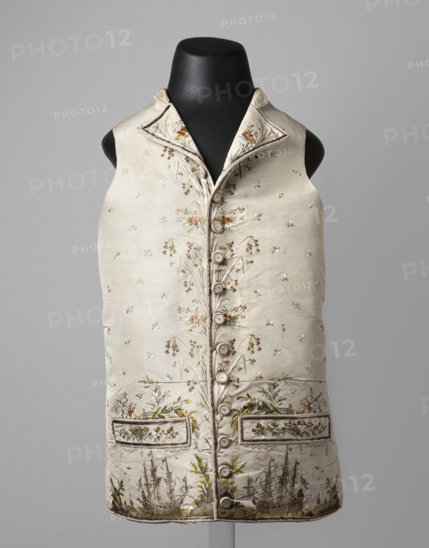 Vest, ships, seascapes, shells, plant ornaments, fashion, men's clothing. Vest made of cream silk grosgrain, straight cut, collarless, with flaps, fastened with covered buttons at the bottom marked by pocket flaps. Richly embroidered front, laced canvas back, silk lining. Embroidery background with small floral motifs; along the fastening are flower sprigs and grass. Chains around the pockets; above the pockets are flowers, a fragment of a stork's nest, and a seagull. Sea vegetation and shells adorn the pocket trim. Beneath the pockets is a fragment of a seascape with two three-masted ships and a small ship in the background. Flat embroidery using satin, laid, and knotted stitches; untwisted and twisted silk yarn. Predominant colors: green, gray, and salmon. 1780s, Silesia and France, garment, length 70 cm., A sleeveless, waist-length garment displayed on a black mannequin, made from a light-colored fabric with delicate floral embroidery and decorative stitching; the front has a row of...