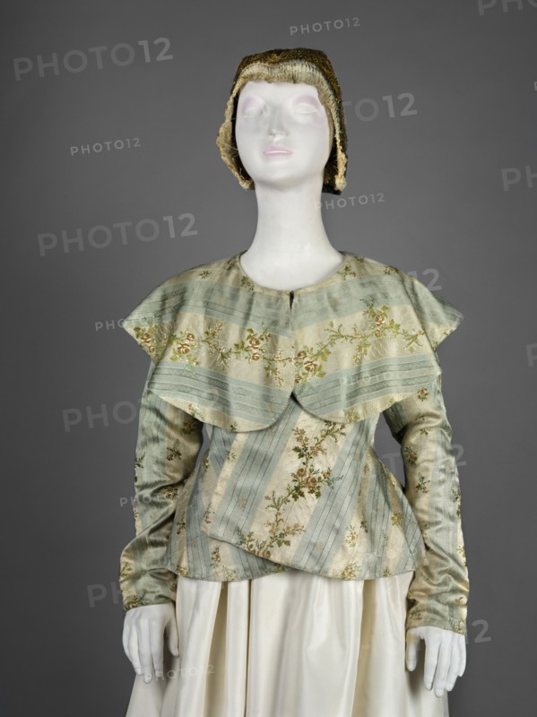 Women's caraco 18th century, blue and white silk brocaded and embellished with rose branches. Straight-cut front fastened with hooks, slightly overlapping lapels; low neckline finished with a large turn-down semicircular collar; long set-in narrow sleeves. Back cut with triangular gussets widened at the bottom and waist to create a generous basque/ruffle. Dark blue canvas lining; lace-up waistband at the lining. Inside, under the flaps at the sides, a wide red canvas belt is sewn on and laced at the front. Second variant: cream silk with blue stripes and colorful floral branches, fitted at the top; overlapping lapels with sides sewn on the bias; large turn-down semicircular collar covering the shoulders and falling deeply into the back; long set-in narrow sleeves cut in a curve at elbow height; back fitted at the waist and widened below by triangular gussets. Europe, 1770s. Garment; length 56.5 cm, bottom circumference 249 cm. Maker: unknown. Creator name: Józef Brandt 1841–1915 noted....
