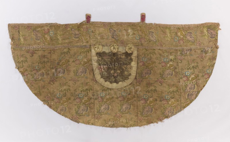 Church cope. Skirt made of olive silk with a warp satin background, brocaded in approximately 13 shades of color. Complex weave structure with a large, elaborate repeat showing a large floral arrangement surrounding a chinoiserie genre scene: two figures in caftans and pointed hats — one standing under an umbrella, the other kneeling with arms crossed — set among lush leaves with fanciful, slightly twisted forms, large fully bloomed flowers, and bursting ripe fruit revealing seed-filled interiors. Part of the cope's skirt under the hood has been cut out; that area is covered by a hood of a different fabric of similar color. Pattern motifs with a symmetrical composition displayed against a taffeta-weave background. Paperwork threads: purple, light and dark pink, yellow, light and dark olive, pale celadon, yellow-green olive-brown, light brown, light pink-raspberry, dark pink-raspberry, light salmon, dark salmon, light blue, dark blue. Hood roughly square in shape and lined with linen. P...