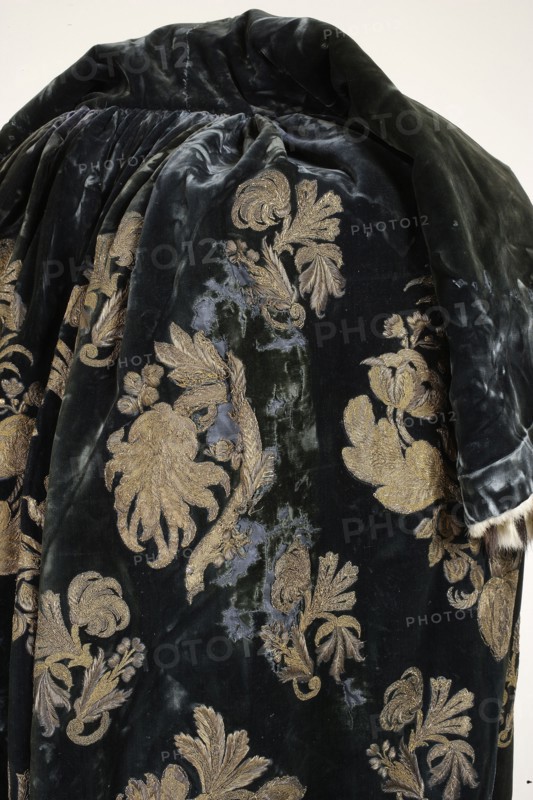 Coronation cloak of King Augustus III, regalia, Augustus III the Saxon King of Poland; Elector of Saxony; 1696–1763. Cloak of dark blue velvet embroidered with silver and gold braided thread and gold lamellar with palmettes. The embroidery is partly directly on the ground, partly appliquéd. The pattern is composed in a repeat format—motifs rhythmically repeated across the entire surface. The repeat consists of larger appliquéd and smaller palmettes embroidered directly onto the cloak. Elaborate larger and smaller palmette compositions with symmetrical arrangements two motif types surround larger and smaller compositions with asymmetrical branches bearing fanciful flowers and strongly curved stems, tilted right and left three branch types in alternating arrangements. The pattern layout is extended in length, with the pattern width equal to the fabric width. The embroidery motifs resemble silk fabric patterns of the period, including lace-like designs. The garment is edged and lined with...