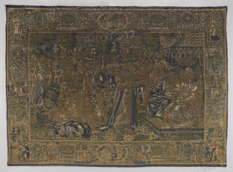 Figural tapestry, tapestries, fabrics, biblical scenes, decorative fabrics, interior furnishings, interior decorations, court scenes, weaving, scenes against a landscape background, borders. In the foreground, on the right, on a throne under a canopy sit two male figures in hats; in front of them stands a woman, behind her a small child, and another woman kneeling. Around them are other figures of women and armed men. In the background is a mountain landscape. Border with plant motifs and female figures; in the upper and lower centers are medallions with small scenes. Colors: green, sand, blue, gray, yellow. 4–5 warps per 1 cm, 10 wefts per 1 cm, wool, silk, wool warp, tapestry technique, numerous visible chains — also used in connecting shades of leaves small color fields and stitched technical slits. 16th century, Flanders, fabrics, height 338 cm, width 462 cm, A large woven tapestry with an ornate border surrounding a central scene, rendered in muted tones of gold, blue, green, brow...