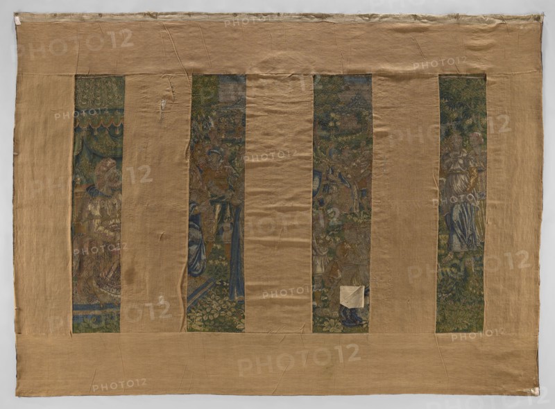 Figural tapestry. In the foreground, on the right, on a throne under a canopy sit two male figures in hats; in front of them stands a woman, behind her a small child, and another woman kneeling. Around them are other figures of women and armed men. In the background is a mountain landscape. Border with plant motifs and female figures; in the upper and lower centers are medallions with small scenes. Colors: green, sand, blue, gray, yellow. 4–5 warps per 1 cm, 10 wefts per 1 cm; wool, silk, wool warp, tapestry technique, numerous visible chains—also used in connecting shades of leaves small color fields and stitched technical slits. 16th century, Flanders. Height 338 cm, width 462 cm., A large rectangular textile is shown with a wide tan border surrounding a central area divided into vertical strips; the border and backing fabric are light brown and beige with visible creases and stitched seams. Within the border there are a few narrow vertical panels of richly colored woven scenes featu...