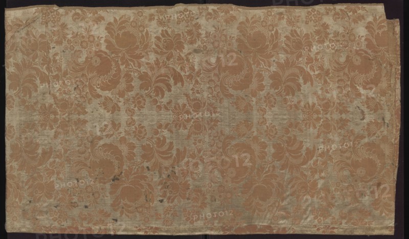 Fabric fragment. Fragment sewn from two salmon-white damask-type fabrics promoted stripes, differing slightly in pattern and ply width. 1. Damask effect achieved by different colors of warps and wefts. Pattern in mirror symmetry. Tiny blossoms spill out from large, blooming peony-type flowers. White taffeta background, salmon pattern - gros de Tours. Report: height 29 x width 49.5 cm panel; edge width 0.5 cm. 2. Damask effect achieved by different colours of warps and wefts. Pattern in mirror symmetry. Large fruit and blooming flowers, lace motifs resembling combs of French needlepoint lace. White taffeta background, salmon pattern - gros de Tours. Report: height 38.5 x width 50.5 cm panel; edge width 0.4 cm. Dated 1735–1745, France. Overall fabric fragment: height 98 cm, width 97 cm. Materials: silk, pseudo-damask; patterned floral and plant motifs; stripes; preserved selvedge, ply width, and pattern repeat., A large rectangular piece of fabric with an overall floral damask pattern sh...