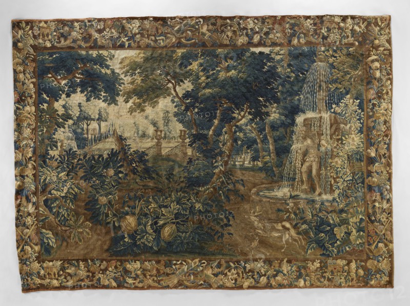 Tapestry - verdure, Flowers, floral ornaments, dogs, deer, tapestries, interior furnishings, park scenes, decorative tapestries, park scenes with architecture, interior decorations, animals, fountains, borders, trees, garden scenes, landscape scenes, parks, park sculptures, gardens. On the right, a fountain with two piled goblets, one supported by Atlas; in front of the fountain a dog and a deer. In the center foreground, a bush with pumpkin fruit. In the background on the left, garden architecture; in the center and right, trees. Border with floral motifs, fruit, and musical instruments. Colors: green, blue, brown, ochre, yellow. Late 17th century, Flanders. Fabric. Height 415 cm, width 297 cm., A woven scene shows a wooded landscape with a group of large trees in shades of deep blue, green, and brown, with areas of beige and tan suggesting sky or distant ground. In the right foreground a sculpted fountain with cascading streams of pale blue and white water stands on a circular basin,...