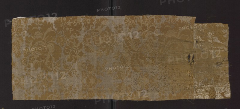 Fabric fragment, fabrics, fragments of silk fabrics, patterned fabrics, floral patterns, stripes, patterns with a symmetrical composition. A type of two-color damask in olive and white. Weave construction: two-color warps olive and white. Background: derivative of a plain weave olive with a sub-ornament promoted with olive warp threads and sparse weft interlacing a type of grodetur. Pattern: derivative of a plain weave white wefts. Decoration: symmetrical in a mirror-like arrangement with axis of symmetry at center of the panel; branches of stylized flowers dominated by large, blooming peonies; sub-ornament features floral and lace motifs. Colors: olive background, white motifs. Wefts: white and olive. Warps: white and olive; leading—olive. Panel width: ?; edge width: 0.4. Report: height 40 cm, width ?; 1st half of the 18th century, France ; fabrics, height 65 cm, width 24 cm., A rectangular piece of patterned fabric with a floral damask design laid against a dark background; the fabri...