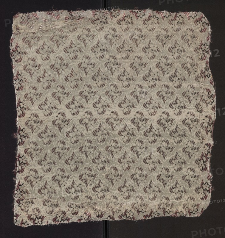 Fabric fragment, fabrics, fragments of silk patterned fabric with floral motifs. Dimensions of the fragment: 7.5 x 7 report and overall height 51 cm, width 48 cm. Colors: white background with motifs in pale pink, plum, and black. 2nd half of the 18th century, France., A square piece of woven fabric with a repeating floral and curving motif covering the surface, displayed on a dark background. The fabric shows a textured, raised pattern in pale beige or off-white threads against a muted darker backing that appears dusky purple or brown. Along the edges there is a border with small floral shapes and frayed threads, showing hints of darker purple and black. The woven pattern creates a subtle contrast between the light raised design and the deeper, shadowed areas, and the fabric edges are slightly irregular with loose fibers visible.