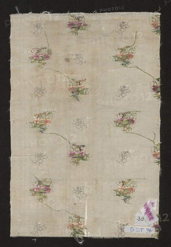 Fabric fragment. Fragment of silver-and-white silk fabric with miniature flower bouquets and floral patterns. Report: length 21.5 cm; overall height 37.5 cm, width 24 cm. 2nd half of the 18th century, France. Materials: silk; patterned fabric., A rectangular piece of light beige fabric with a repeating floral motif scattered across it, showing a few clustered flowers in shades of pink, green, and muted purple with thin green stems, and several faint outline floral sketches in gray; the fabric has a slightly uneven texture and some small stains and worn spots, frayed edges at the top and bottom, and a dark background surrounding the fabric that contrasts with its pale color.