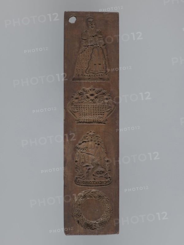 Double-sided gingerbread mould. Obverse: four motifs — at top a female figure in a long patterned dress with a low neckline; below, a basket of flowers; below that, a seated young naked man with long hair sitting among flowers and smoking a pipe, with a skull and crossbones at his feet inscribed MEMENTO MORI; at the very bottom a wreath woven from leaves and flowers. Reverse: five images of infants in patterned swaddling clothes. Materials/subject: gingerbread mould; gingerbread; decorative folk motifs; wreaths; female figures in rich dresses; Transience personification; floral decorations; allegorical representations; infants. Double-sided, rectangular mould. 19th century. Province of Silesia 1742–1918. Form dimensions: height 36.5 cm; width 8.8 cm; depth 1.5 cm. Creator: unknown., A tall narrow wooden panel with a vertical arrangement of carved motifs, showing a carved figure of a person in a dress near the top, a decorative basket of flowers below that, a seated figure with flowing ...