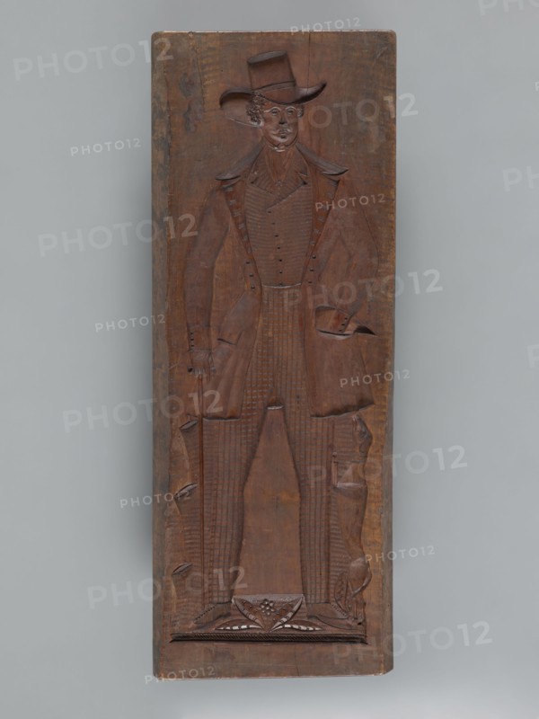 Double-sided gingerbread mould. Side A: figure of a lady; Side B: figure of a bachelor. Woodcarver or gingerbread, Rectangular form, 19th century dated 1842. Silesia Province of Silesia, 1742–1918. Height 84.5 cm, width 32 cm, depth 4 cm. One side: male figure in a high hat with a cane, outfit from the first half of the 19th century—frock coat, coat, checked trousers; a dog at his feet standing on its hind legs. Other side: female figure wearing a decorative bonnet and a long patterned dress with numerous ruffles and ribbons, holding a fan and a handbag in her right hand and a bunch of feathers in her left. Under the legs of both figures is plant decoration. Carved on the edge: decorative letters ACL a. P, initials of the maker or owner of the form. Folk motifs, floral ornaments, decorative art; used as a mold for gingerbread., A carved wooden panel shows a full-length relief of a standing figure wearing a tall brimmed hat and a long coat with wide lapels, with carved details indicatin...