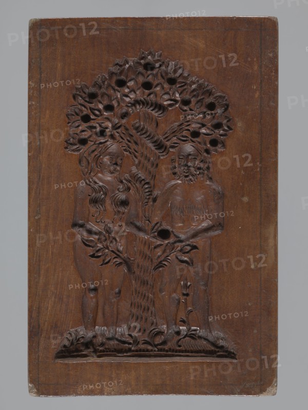 A single-sided gingerbread mold with the image of Adam and Eve in paradise;, Single-sided, rectangular mold depicting naked figures of Adam and Eve standing under the Tree of Knowledge with numerous fruits; Eve gives Adam an apple and a snake is wrapped around the tree. Gingerbread; decorative folk motifs; figurative biblical/religious scene. 19th century, Province of Silesia 1742–1918. Mold; height 20.5 cm, width 13.8 cm, depth 2.5 cm., A carved wooden panel showing a relief of two human figures standing on either side of a tree with a twisting trunk and a canopy of stylized leaves with round holes; the figure on the left has long wavy hair and the figure on the right has a beard and shorter hair, both shown with minimal clothing and hands near the tree; the base shows carved ground details and small plants; the panel is a medium to dark brown wood with visible grain, slightly lighter worn edges, and small scuffs and scratches, set against a neutral gray background.