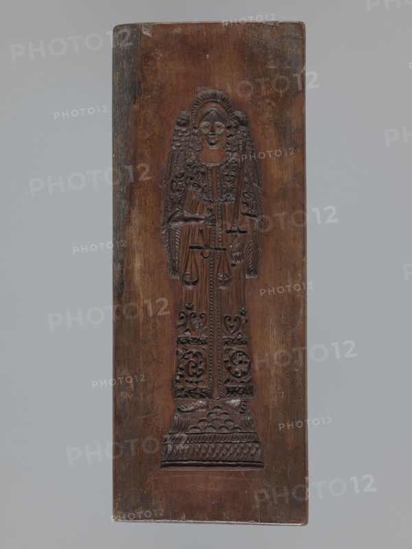 Double-sided gingerbread mould. Obverse: rectangular floral and geometric ornament; a rectangular decorative motif containing a rosette and stylised plants. Reverse: image of the Archangel Michael in a long patterned robe decorated with a plant twig motif, holding scales in his right hand and a sword in his left; at the feet a geometric-plant ornament. Date engraved on the edge: 1806, with the letter S against the background of an anchor mark of the woodcarver or gingerbread maker., woodcarver or gingerbread maker; gingerbread mould; folk-style decorative art with religious motifs; angels, figurative scenes, Archangel Michael iconography; Silesia, Province of Silesia 1742–1918. Form: bas-relief. Dimensions: height 11.6 cm; width 30.5 cm; depth 3 cm., A rectangular wooden panel with a carved upright figure in relief centered on it, showing a person with stylized hair and wings, wearing a long patterned garment with ornate carved details and standing on a patterned base; the wood shows n...
