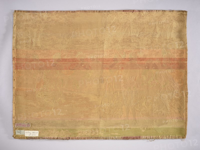 Jacquard tapestry by Mariano Alonso Pérez 1857–1930, co-created by an unknown manufacturer. Depicts ladies and gentlemen in Louis XVI–era costumes watching a lady jumping rope, set in a park landscape. No border. Monochromatic colors in shades of beige and ochre. 19th/20th century, Europe. Materials: fabrics; height 73 cm, width 101 cm., A rectangular woven textile laid flat against a light background, showing a faded overall yellow-beige color with horizontal bands of muted orange and pale green across its width; the fabric surface has a subtle raised pattern depicting indistinct figures and foliage in slightly lighter and darker shades of the base color, with fringed short edges and stitched borders visible along the sides; a few small paper labels are attached near one corner showing contrasting pale and darker tones.