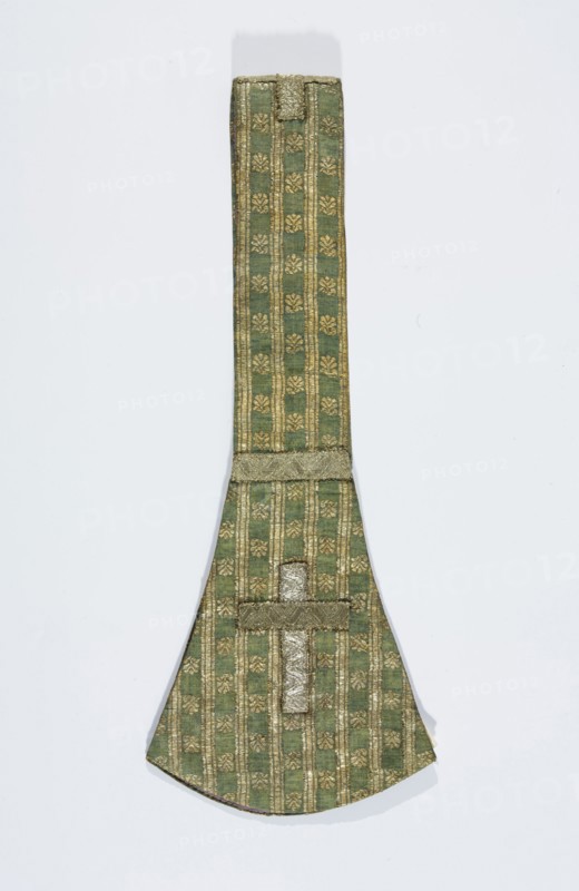 Maniple, liturgical vestment, silk fabric with a fine pattern of stylised floral motifs between gold stripes; lined with linen. Crosses on gold galloon paddles. Fabric background in simple weave warp celadon, wefts blue, brocaded with silver metal thread with a loose braid on a white silk base. 18th century, Grodno, Poland. Length 83 cm, width 16 cm., A long narrow textile object with a wider rounded end, shown against a pale background; the fabric is green with a repeating decorative pattern in metallic gold forming vertical stripes and small floral-like motifs; there is a horizontal band of textured metallic trim near the wider end and another strip of metallic trim forming a short cross-like shape on the rounded section; the overall colors visible are green and gold with subtle variations in shading and a soft shadow beneath the object.
