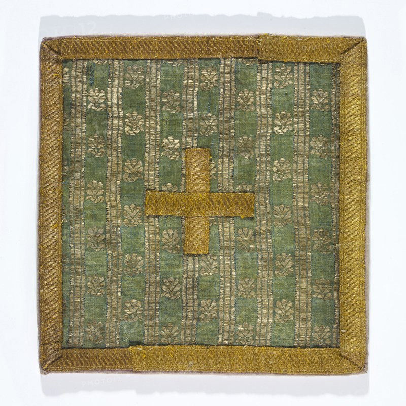 Pall of silk fabric with a fine pattern of stylised floral patterns between gold stripes. Lined with linen. The edge is trimmed with gold galloon. Fabric: background simple weave warp celadon, wefts blue, brocaded with silver metal thread with loose braiding on a white silk base. 18th century. Grodno, Poland. Liturgical vestment. Height 18 cm, width 17 cm. Maker: Pall, unknown., A square textile panel with a green background patterned with vertical stripes and a repeating floral motif in gold tones, bordered by a textured gold trim; a gold cross-shaped applique is centered on the panel.