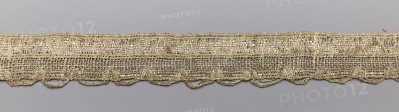 Gallon-lace, galloons haberdashery, origin unknown, haberdashery, 18th/19th century, France, fabric, width 2.7 cm, length 73 cm, A narrow horizontal textile strip lies against a smooth background, showing an open, loosely woven structure with a decorative lower edge of looped scallops; the material has a metallic sheen and appears gold in color, with the background visible through the mesh in gray tones, and some slight variations where threads catch the light giving brighter and darker golden highlights.
