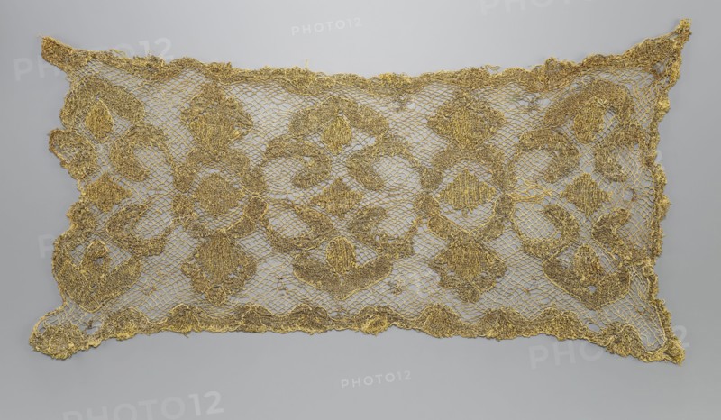 Fragment of lace, lace, 17th/18th century, Belgium, fabric, lace, width 34 cm, length 67 cm, A rectangular lace textile displayed flat against a pale gray background, with an open mesh ground and an ornate repeating floral and geometric pattern worked in a metallic golden thread; the lace has scalloped irregular edges and a delicate net-like structure, with several larger circular and diamond-shaped motifs interconnected by smaller curving elements, and the overall palette shows gold against light gray.