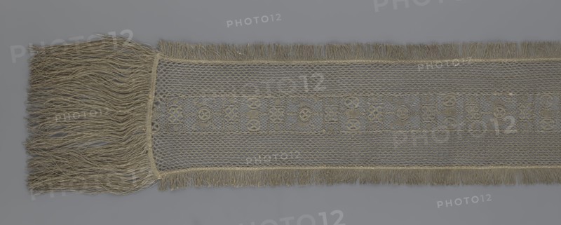 A so-called Saxon lace belt, lace, belts, clothing accessories, men's clothing, clothing, fashion, provenance unknown. The central part is a continuous belt with a geometric ornament; among the motifs is a circle containing an hourglass. The side belts of similar width are permanently connected. The entire belt is trimmed with fringe. 17th/18th century, Poland; lace; height 270 cm, width 25 cm., A long woven textile with fringed ends displayed horizontally, showing a dense group of long loose fringe on the left and shorter fringe along the top and bottom edges; the central band features a delicate mesh-like pattern with a narrower decorative strip of repeating geometric openwork motifs; visible colors include shades of beige, tan, and gray across the fabric and fringe.