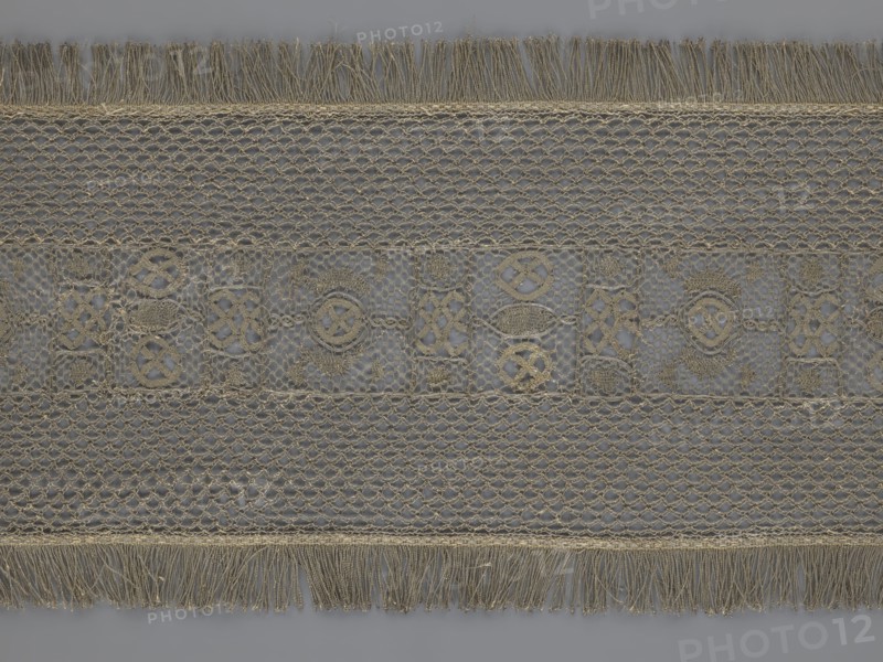 A so-called Saxon lace belt, lace, belts, clothing accessories, men's clothing, clothing, fashion, deposit provenance. The central part is a continuous belt with a geometric ornament; among the motifs there is a circle containing an hourglass. The side belts of similar width are permanently connected. The entire belt is trimmed with fringe. 17th/18th century, Poland. Lace, clothing accessories, clothing. Height 270 cm, width 25 cm., A wide horizontal strip of lace with a repeating openwork pattern in beige and gray tones, featuring a central band of decorative motifs set against a translucent gray background, flanked by two bands of netlike lattice, with fringed edges at the top and bottom made of loose beige threads.