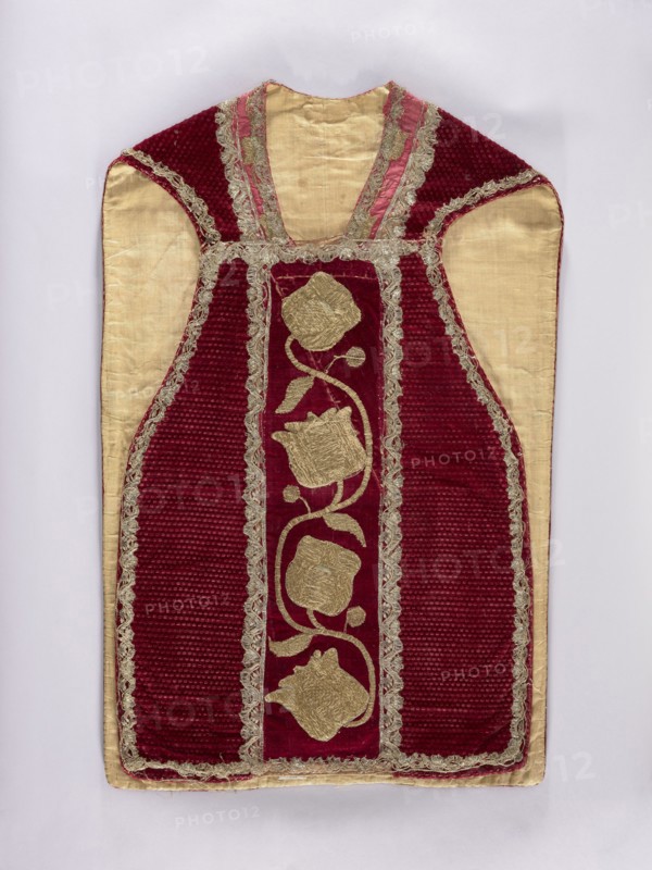 Chasuble, Liturgical vestment, 17th century end of 17th century - embroidery. Central column embroidered with gold on a backing; sides made of pressed velvet. In the columns: smooth velvet with sewn-on gold embroidery on a backing with a thick floral tendril. Trimmed with narrow silver bobbin lace. Cotton lining. Neckline of red silk fabric. Embroidery: metal thread; embroidery laid and flat on metal thread backings gold-colored plate woven on linen yarn? held with linen yarn. Leaves, stems, and buds embroidered directly on velvet; flower chalice embroidered on a separate linen canvas backing and appliquéd. Materials: fabric from Italy; origin: Poland. Function: liturgical vestment. Dimensions: length 107 cm, width 65.5 cm back., A garment laid flat on a pale background with a rich red velvet central panel and side panels, framed by metallic gold trim and lace; the inner fabric is a light beige or cream color, visible on the shoulders and sides. The red velvet areas have a ribbed textu...