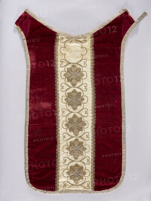Chasuble, liturgical vestment, 18th–19th century, Poland. Back: sides of smooth dark red velvet; central column of white damask with floral patterns and braid and sewn-on stars of the Order of the White Eagle, bearing the inscription Pro Fide Rege Lege one of six stars is missing. Embroidery between the stars with thin thread; silver galloon; cotton lining. Front: central column of white damask covered with silver and gold thread embroidery featuring stars and crosses with a Latin inscription; trimmed with silver braid. Damask with floral and braided patterns. Length 122 cm, width 64 cm back., A single garment laid flat with a vertical design, featuring a central creamy panel with decorative raised motifs framed by metallic trim, flanked by wide deep red velvet panels and edged all around with a pale metallic border; the central panel contains a vertical sequence of ornate floral-like medallions in muted gold and beige with swirling embellishments, and the red velvet shows areas of she...
