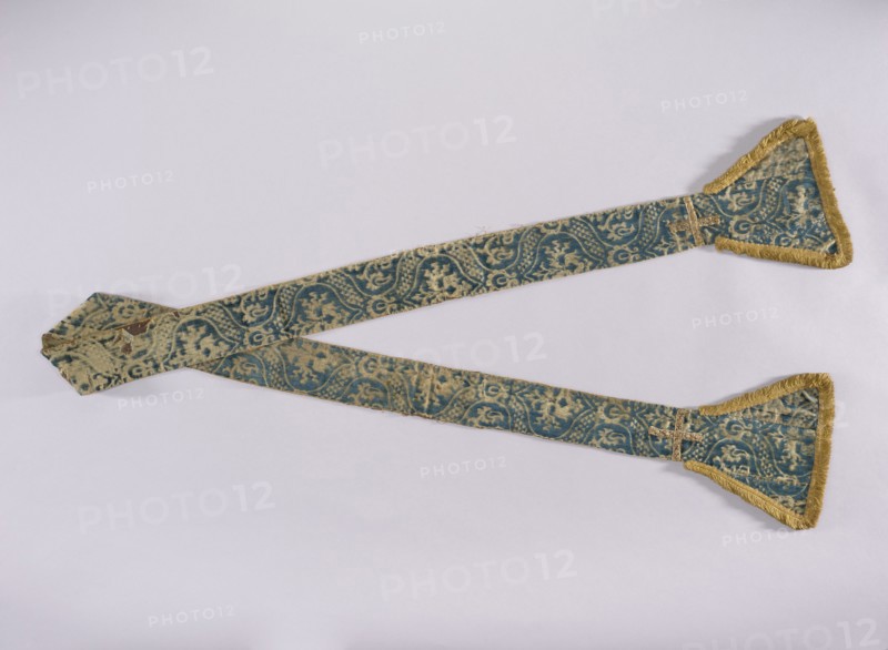 Stole, church paraments; embroidered with flowers, leaves, and crosses; liturgical vestment with plant ornaments; sacred art; for churches and chapels furnishings; widened trapezoidal ends trimmed with a short yellow cotton fringe; lined with silk fabric; 15th century, Genoa, Italy; height 236 cm, width 21 cm., A long decorative fabric band laid out on a pale background, with a pair of tapered ends each finished with triangular flared sections trimmed in fringe; the fabric shows a repeating ornate pattern in teal and beige with areas of wear and faded color, and the fringe and some edging are a golden yellow; the band crosses near one end and has a small sewn patch visible where layers overlap.