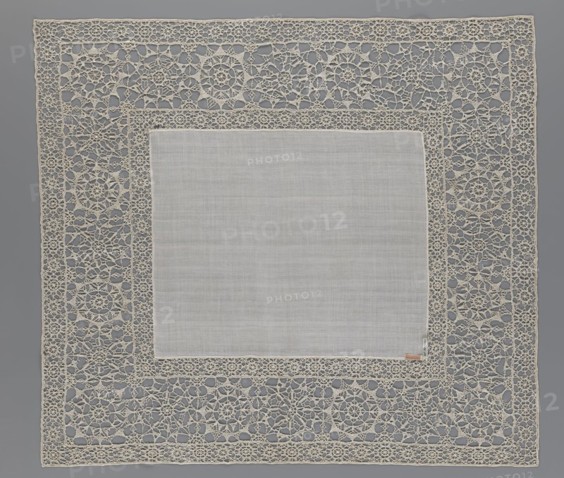 Doily, geometric ornaments, rosettes ornament, doily with smooth center. Edge made of white linen lace with rosette motifs: large rosettes in the center and rows of small rosettes on the edges; punto in tela lace; ca. 1600, Italy. Materials: lace, fabric. Dimensions: height 79 cm, width 70 cm., A square fabric piece with a plain central panel in light gray surrounded by an ornate openwork lace border in off-white and cream tones, the lace forming repeating circular and floral motifs and interconnected geometric patterns, all set against a medium gray background.
