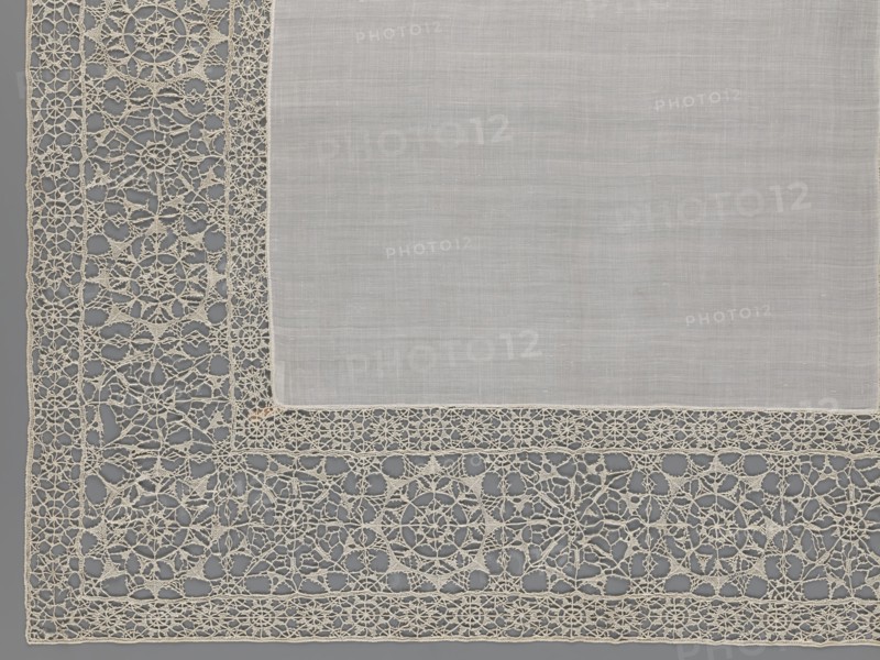 Doily, geometric ornaments, rosettes ornament, doilies, smooth center. Edge made of white linen lace with rosette motifs: large rosettes in the center and rows of small rosettes on the edges, punto in tela lace, ca. 1600, Italy, lace, fabric, height 79 cm, width 70 cm, A corner of a rectangular, light-colored fabric panel with a plain central area and an ornate openwork border; the plain area is a soft, pale off-white with a fine woven texture, and the border is an intricate lacework in a slightly warmer cream tone featuring circular motifs, radial patterns, and interconnected looping threads set against a muted gray background.
