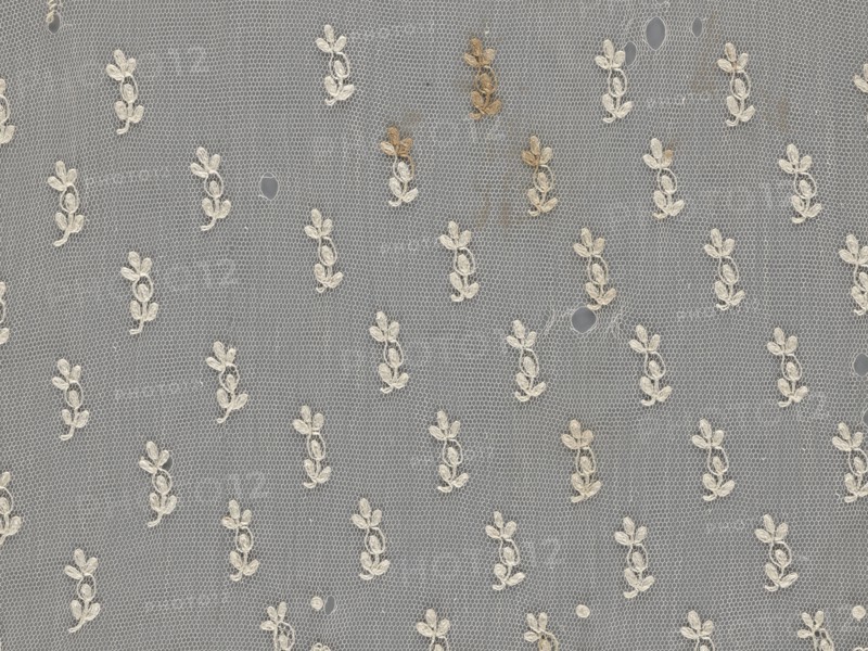 Lace fragment — shuttlecock;, Mid-19th century, France. Lace clothing accessory fashion. Lower edge: semicircular serrations bordered with fine serrations with geometric ornament. From the semicircular serrations upwards: a floral ornament repeating with a twig motif in triangular divisions. Above this, a small twig in a regular projection. Material: lace. Width 42 cm; length 430 cm., A sheer net fabric with a repeating floral motif embroidered in off-white thread over a gray background, showing a few small holes and a group of light brown stains near the top, with the netting forming a hexagonal mesh pattern throughout.