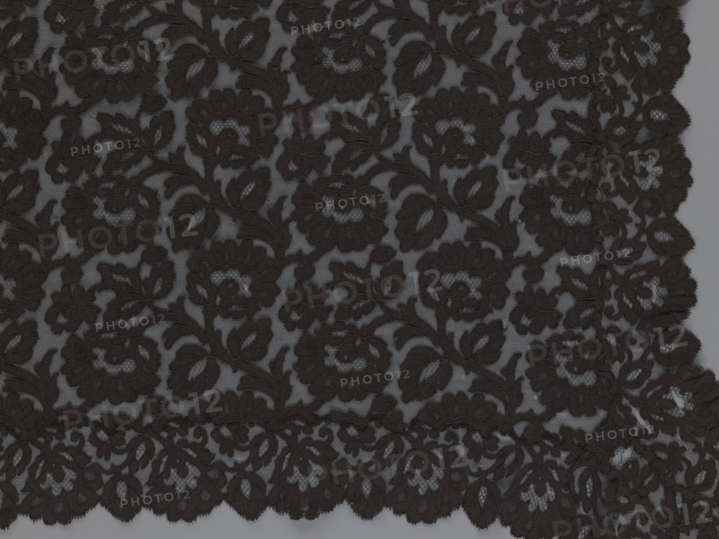 Cape, lace, in the form of a square with two wide, elongated lace ties. Continuous floral ornament with a motif of a large, asymmetrical flower sprig. Raised edge, a strip of floral edge ornament made separately and sewn on. 2nd half of the 19th century, France., Height 97 cm, width 168 cm., A close-up view of a textured black lace fabric with an ornate floral pattern, showing a repeated design of flowers and leaves on a sheer grayish background; the lace has scalloped edges and intricate openwork, with visible threads and raised embroidered areas in black against the lighter gray base.