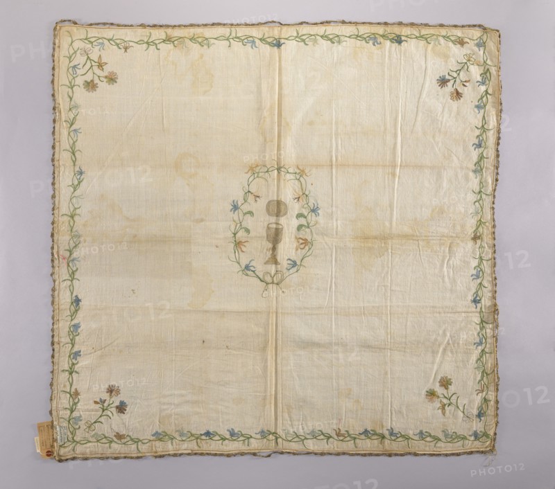 Church napkin made of linen fabric with a rare plain weave. Embroidered with chain stitch using colored silk and gold thread also pierced. In the center, in a wreath of flowers tied with ribbon, is a gold chalice, and above it a gold oval—probably a patera, not a host. In the corners are floral sprigs tied with a ribbon with double loops. A floral tendril runs around the edges. The flowers are stylized, not decorative. Flower colors: green, brown, blue, sky blue, pink, tobacco. Narrow gold lace sewn around the edges now very damaged. Fabric density: 30 weft threads, 23 warp threads per cm. Second half of the 18th century, Poland. Materials: linen, silk, gold thread. Dimensions: height 100 cm, width 105 cm. Subject: church paraments, sacred art; motifs: flowers, leaves, plant ornaments., A large square cloth with a pale off-white background that shows faint creases and light stains, bordered by a decorative vine-like embroidery in green threaded along the edges with small floral motifs ...