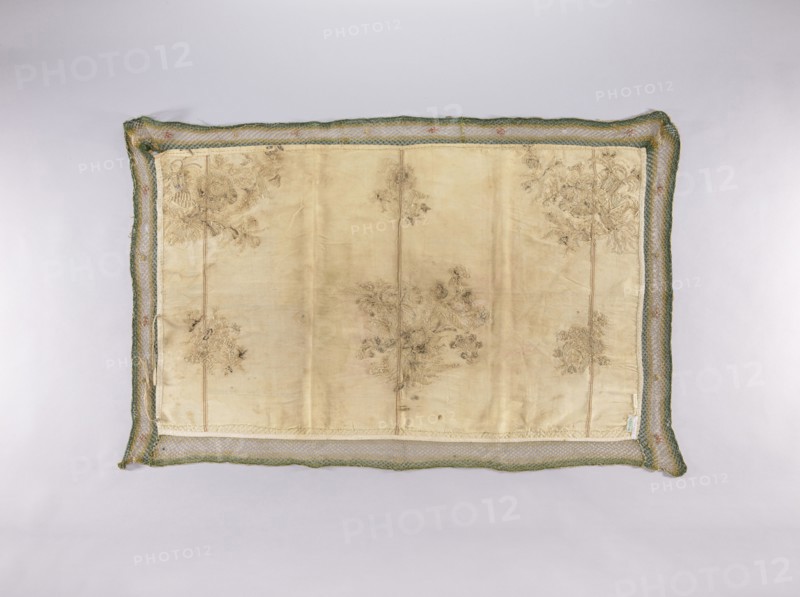 Wall hanging of rep fabric sewn from many fragments, embroidered with beige, cream, ash, and brown silk thread with flat stitches, and with silver thread and plate with laid stitches — in places on a backing of thin string. In the center of the lower edge and in the upper corners are bouquets composed of large and small flowers, fruit, and cornucopias. In the lower corners and in the center of the upper edge are smaller floral sprigs. Trimmed with a wide mesh ribbon with sewn-on flowers. Tie strings are sewn onto the narrow edges. Floral motifs; plant ornaments; flowers and leaves; sacred art; churches and chapels furnishings. Piece width 49 cm; fabric density 23 weft threads and 35 warp threads per cm; brown selvedges; height 73 cm; width 120 cm; 2nd half of the 18th century; Poland., A rectangular embroidered fabric panel lies flat against a light background, framed by a loosely woven border with a braided texture; the panel center is a pale beige or ivory silk with visible creases a...