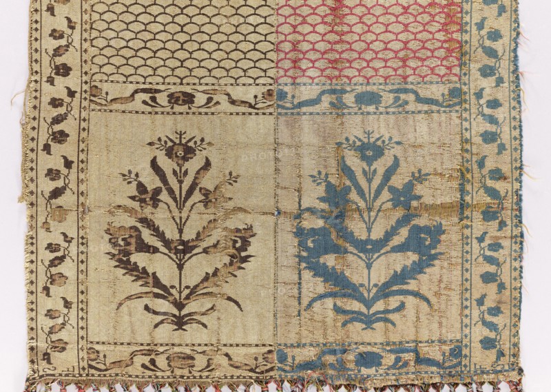 Kontusz belt, Flower bushes ornament; solid belt with carp-scale ornament; four-sided belt with plant ornaments. Polish kontusz belt, men's clothing accessory. Bipartite heads with flower-bush motifs; carp-scale pattern continues. Edge with motif of small flower-sprig tendrils. Colorful silk fringe, sewn on. Colors: gold, brown, silver, and blue. Signed at the bottom of the heads: FS lying. 2nd half 18th century. Possibly Slutsk, Grand Duchy of Lithuania 1569–1795 / Poland. National costume accessory. Length 356.5 cm, width 28.5 cm., A woven textile with a patchwork layout showing a few vertical panels and a group of rectangular sections, featuring floral and scallop motifs; the left side has darker brown floral patterns on a beige background with a narrow border of small repeating floral elements, the right side shows similar floral motifs in blue on a beige ground with a vertical blue vine-like border, the top right contains a scalloped pattern in pink on beige, and the top left has ...