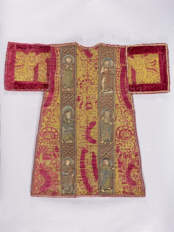 Half of a dalmatic. Preserved half of a dalmatic made of red, patterned, large-scale velvet with pomegranate and thistle flower motifs brocaded with metal thread. Two panels with figures of saints are sewn onto the fabric, three in each stripe. Figures of saints with attributes placed in semicircular arcades: on the right panel — St. John the Evangelist with a chalice, St. John the Almsgiver with a staff and a book, a deacon with a book; on the left panel — St. John the Baptist, a very damaged saint with a halberd, a saint with a spear possibly St. Maurice. Embroidery in metal threads Cypriot gold and multicolored silk; stitches include flat laid on a thread base, banner, Burgundy shaded gold, Cologne, cord, and split stitches. The figures of the saints are executed on a separate base and applied; faces and hands are made of applied silk satin. Metal threads held with silk yarn two or three threads each. c. 1500, Italy fabric. Liturgical vestment. Height 89 cm, width 95 cm., A garment ...