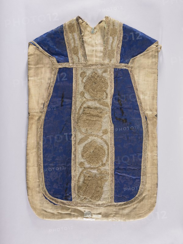 Chasuble, gift; tulips, plant ornaments, floral ornaments, flowers; liturgical vestment church paraments, sacred art, 17th century, Poland. The sides of the chasuble are made of a semi-silk navy-blue damask fabric with a motif of twisting floral sprigs. The columns have a tendril motif with schematic representations of tulips and roses, embroidered with metal thread: silver in the background, gold in the ornamental section. The edges and internal divisions are trimmed with metal galloon. Cotton lining. Embroidery: gold metal thread laid on a backing of thick linen canvas. Background, leaves, and buds — flat laid embroidery; flower cup and stems — raised laid embroidery on a backing of linen threads. Gold threads: gold-colored metal plate in ornamental parts and silver-colored metal plate background woven on a linen base; threads attached to the base with linen yarn. Length 114 cm, width 66 cm back., A garment laid flat with a long rounded bottom and a V-shaped neckline, showing a centr...
