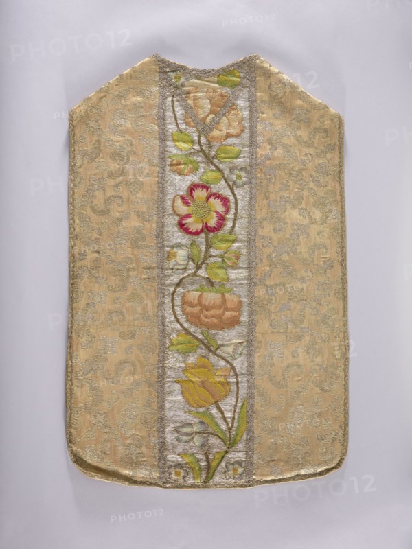 Chasuble, Floral and plant ornaments with flowers and leaves; columns embroidered on a silver background with large flower motifs in yellow, cherry red, green, and blue. Unstitched and trimmed with silver lace braid; cotton lining. Side fabric: cream silk brocaded with gold thread with stylized twigs and leaves. France, 3rd quarter of the 17th century fabric; 18th century, Poland embroidery. Liturgical vestment. Length 101 cm, width 67 cm back., A rectangular textile panel with a pointed top edge displayed against a pale gray background, featuring a central vertical embroidered panel with a winding stem bearing a group of stylized flowers and leaves, surrounded by a patterned brocade field; colors visible include gold and beige in the background fabric, green in the leaves, yellow and orange in some flower petals, pink and red in a central flower, and silver-gray in the narrow vertical band framing the floral embroidery.