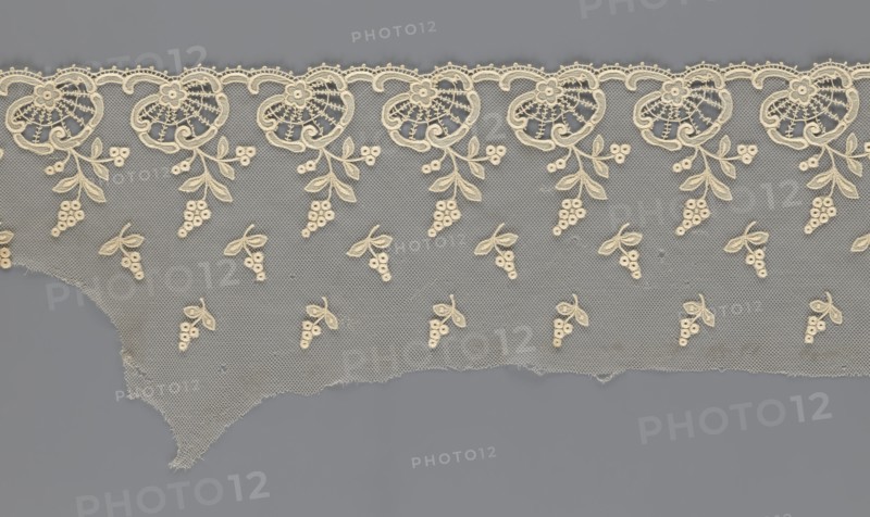 Fragment of lace, lace with plant ornaments, slightly serrated lower edge, shell motifs with sprouting twigs and projections of smaller twigs above, 2nd half of the 19th century, Europe, lace, width 20 cm, length 161 cm, A length of delicate lace fabric with an open mesh background in gray and cream hues, featuring a scalloped top edge with a repeating floral motif in cream; dangling from the scalloped border are cream embroidered leaf-and-berry sprigs, and a scattered pattern of small cream berry-and-leaf clusters fills the mesh area; the lower edge is irregular and frayed, and the overall colors visible are gray and cream.