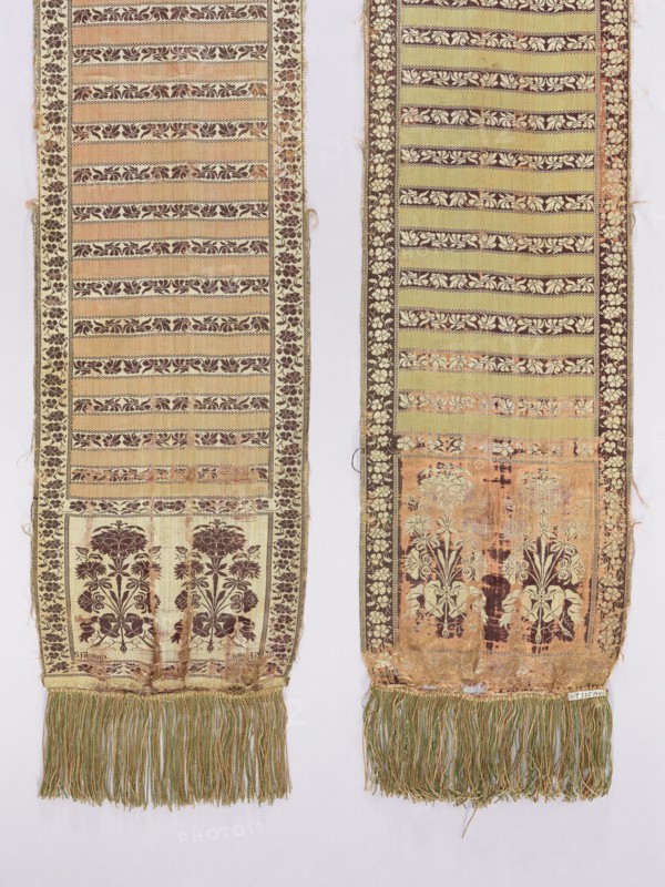 Kontusz sash, Szczepan Filsjean Manufactory Kobylka; belt manufacturer; 1787–1794. Silk kontusz sash, double-sided. Bipartite heads with bouquets of flowers carnations rooted and tied with ribbon, alternating with smooth stripes and floral twigs. Trimming with floral twig. Colors: brown, cream, olive and crimson. Sew-on silk fringe in green, straw and ochre. Ornament - Heads: two floral bouquet motifs each. - Middle: alternating transverse shelves, plain and with a floral tendril motif. - Borders: vertical and horizontal with a tendril motif, borders: checkerboard. Colors - Present: cream-pink background of heads, borders and shelves with tendril, brown ornament; plain crimson-pink shelves. - Reverse: right, except for plain green shelves. Signed in the corners of one of the heads, under the main motifs: S. Filsjean. Weave density: approx. 17/48 x2. Bouquet motifs similar to motifs in other contemporary belts. Date/place: 1787–1794, Kobylka, Poland. Function: clothing accessory for nat...