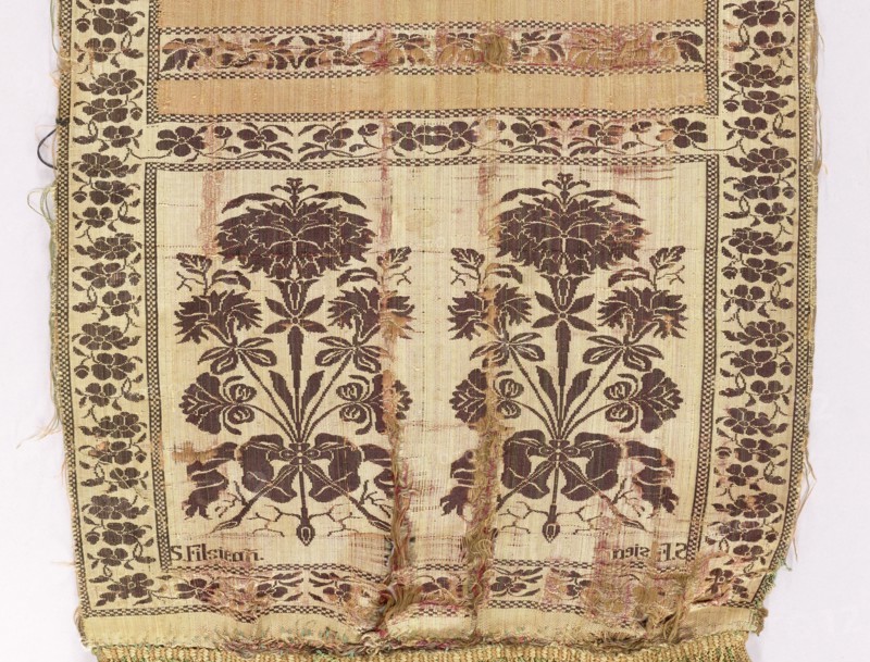 Kontusz sash, Szczepan Filsjean Manufactory Kobylka; belt manufacturer; 1787–1794. Silk kontusz sash, double-sided. Bipartite heads with bouquets of flowers carnations rooted and tied with ribbon; alternating smooth stripes and floral twigs. Trimming with floral twig. Colors: brown, cream, olive and crimson. Sew-on silk fringe in green, straw and ochre. Ornament: - Heads: two floral bouquet motifs each. - Middle: alternating transverse shelves, plain and with a floral tendril motif. - Borders: vertical and horizontal with a tendril motif, as in the shelves; checkerboard. Colors detail: - Principal: cream-pink background of heads, borders and shelves with tendril, brown ornament; plain crimson-pink shelves. - Reverse: right, except for plain green shelves. Signed in the corners of one of the heads, under the main motifs: S. Filsjean. Weave density: approx. 17/48 x2. Place/date: Kobylka, Poland, 1787–1794. Type: clothing accessory, national costume. Dimensions: length 342 cm, width 28.5 ...