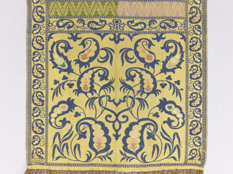 Kontusz belt, Giani I. 19th century. Four-sided kontusz belt with heads composed of two branches bearing bota palmettes in mirror symmetry. Centre: transverse shelves alternating with a tendril with bota motifs and a zigzag ribbon. Edges: tendril motifs like the shelves. Borders: arranged in squares. Colouring: Right side — straw-colored background; ornament of heads, borders, and shelves with tendrils in navy blue and shades of blue and pink; shelves with zigzags half lilac. Left side — colouring of heads, borders, and shelves with tendrils reversed from the right side; shelves with zigzags have a background half straw-colored and half celadon-colored; ornament is lilac. Technique: flaunted and brocaded weave. Weave density: approx. 26 weft threads and 22 warp threads per cm². Function: men's kontusz belt clothing accessory. Date/place of origin: 19th century, Vienna. Dimensions: length 325 cm, width 37.5 cm., A rectangular textile panel with a decorative border and central repeating ...