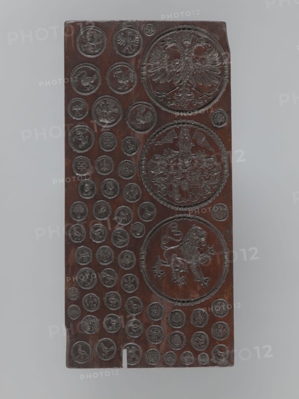 Gingerbread mold with 3 coats of arms and 52 medallions, boards and gingerbread; national emblems, zoomorphic motifs, coats of arms, banners, female busts; decorative art. Rectangular, flat gingerbread mold with representations forming medallions of various sizes, with a wreath-shaped border. Three large medallions, placed one below the other, contain heraldic images: 1. A double-headed eagle under a crown. 2. A quartered coat of arms with a lion, an eagle, a human figure, and the letter W in the fields; a human head in the central field; the shield topped with a crown, above which are a female bust and two banners; decorative lambrequins made of plant twigs flank the shield. 3. A mounted lion facing right. The form's decoration is complemented by 52 small medallions containing images of animals mostly birds, and anthropomorphic, geometric, and plant motifs. 16th–17th century, unknown locality; utility item., A vertical rectangular wooden panel with a dark brown surface carved with a g...