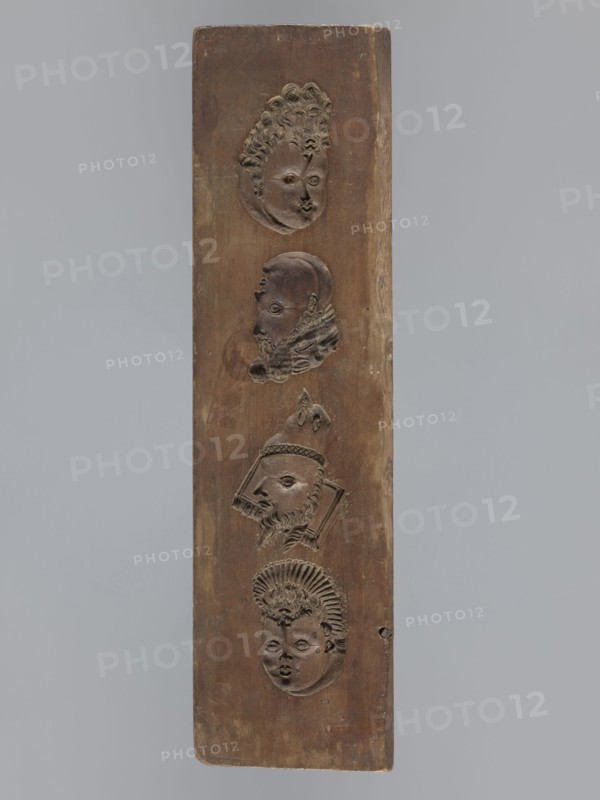 Double-sided gingerbread mould. Obverse: images of four heads; on rotation heads take on male or female appearance in one the male head changes into a goat. Reverse: seven elements in decorative frames: a house roof, a flower, a bird, a plate inscribed IDR / 1763 and another inscribed GFK / 1763, an anchor and cross, decoration complemented by a wreath and flower motif in a medallion. Plant ornaments, human figures, zoomorphic motifs, wreaths, decorative art, religious symbols, inscriptions, folk art. Date: 1793. Region: Silesia Province of Silesia, 1742–1918. Form. Materials: applied art gingerbread mould. Dimensions: height 34.6 cm, width 9.3 cm, depth 2 cm., A vertical rectangular wooden panel with a brown surface displays a vertical arrangement of a few carved human faces in relief, each with distinct hairstyles and facial features; the top face has curly hair and an oval face, the next shows a profile with a beard and textured collar, the middle carving depicts a bearded profile w...