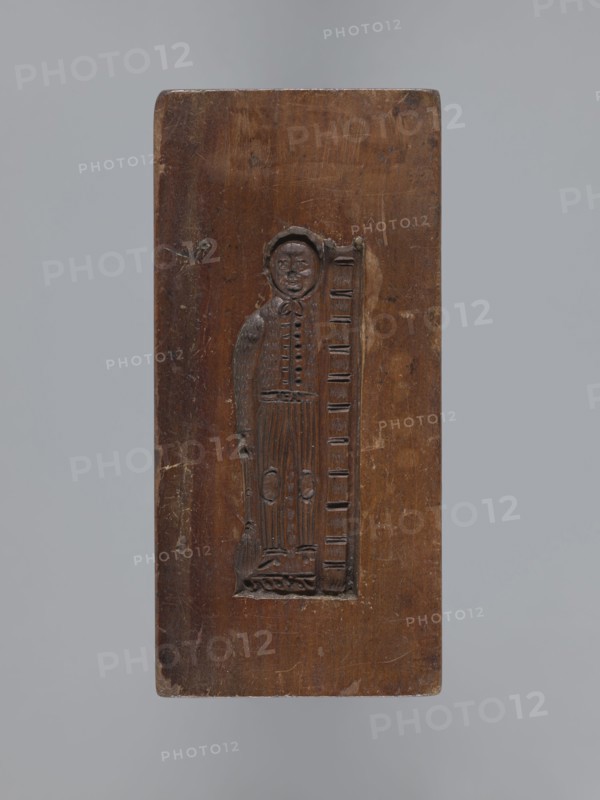 Double-sided gingerbread form. Side A: female figure with a scarf on her head, standing, leaning on a ladder and holding a broom. Side B: baby in swaddling clothes decorated with a geometric ornament. Rectangular shape; on one edge the date 1830 is engraved with the letter S against an anchor and, below it, M mark of the woodcarver or gingerbread maker. Material: gingerbread form wood. Function: form. Style: folk motifs, decorative/applied art. Subject: female figures, children, babies. Maker: unknown woodcarver or gingerbread maker. Date: 1830. Place/region: Silesia Province of Silesia, Prussia; 1742–1918. Dimensions: height 13.5 cm, width 6.5 cm, depth 4.5 cm., A rectangular wooden panel with a carved inset depicting a standing human figure next to a vertical ladder-like element; the panel shows a rich brown wood tone with darker carved lines and lighter worn areas, and the background around the panel is a neutral gray.