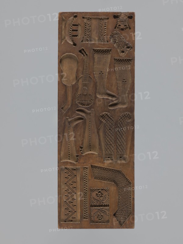 Double-sided gingerbread mould, rectangular, wood, height 29 cm, width 10.5 cm, depth 2.4 cm. Maker inscription on the edge: Glauer: signature of the woodcarver or gingerbread maker and the date j.1827. Dated 1826. One side: twelve small images of animals two horses, two roosters, two crayfish, and two storks carrying babies in baskets and two decorative pipes. Other side: miniature elements including children in swaddling blankets, shoes, footwraps, a cradle, a guitar, and other motifs adorned with plant and geometric ornaments. Decorated with folk, zoomorphic, plant, and geometric motifs; function: form for gingerbread. Silesia Province of Silesia, 1742–1918., A rectangular wooden panel carved with a variety of shallow relief shapes and patterns, showing a few elongated sock-like forms, a guitar-shaped outline, several curved and geometric motifs, and a group of decorative bands and floral-like medallions; the panel surface is brown with darker carved recesses and faint lighter worn ...